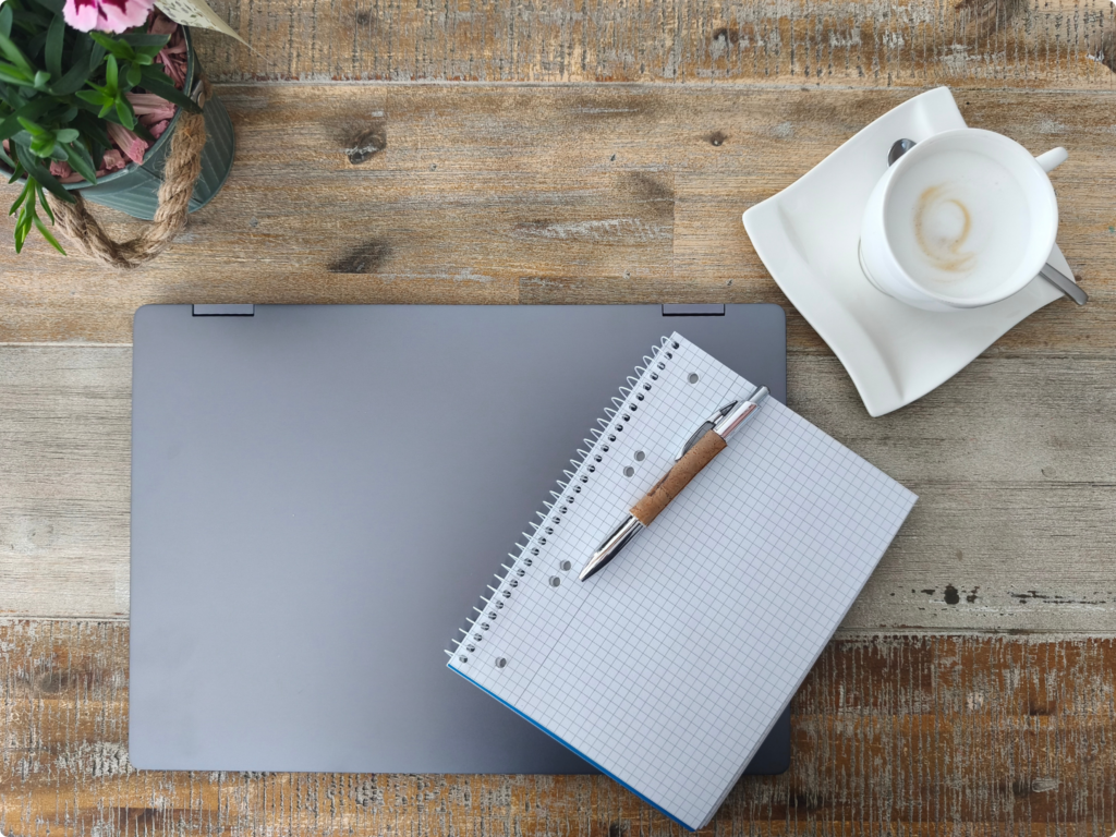 Schreibtisch von oben, auf dem sich ein Laptop, ein Notizblock mit Stift, eine Tasse Kaffee und eine Pflanze befindet, dekoratives Element im Kontaktaufnahmebereich der Webseite