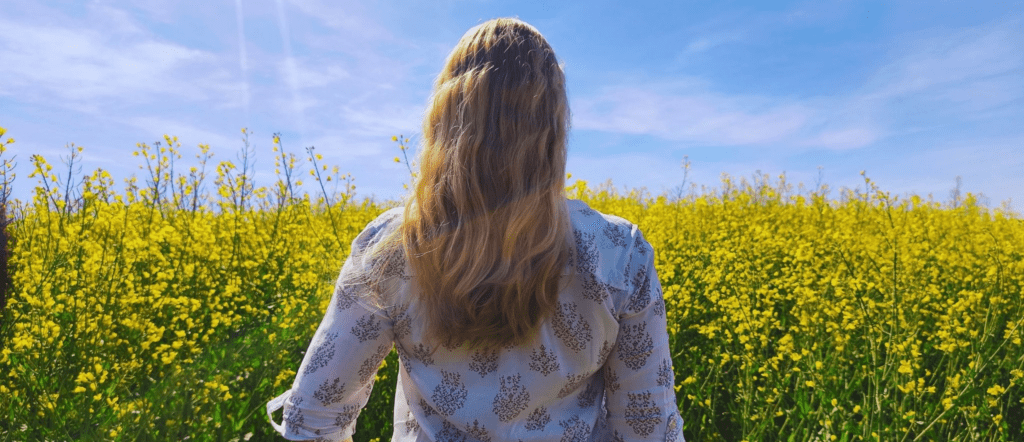 Rückenansicht der Firmeninhaberin Natalie Kuhn mit Blick über ein blühendes Rapsfeld, drückt Naturverbundenheit aus im Webseitenbereich ''Über mich'